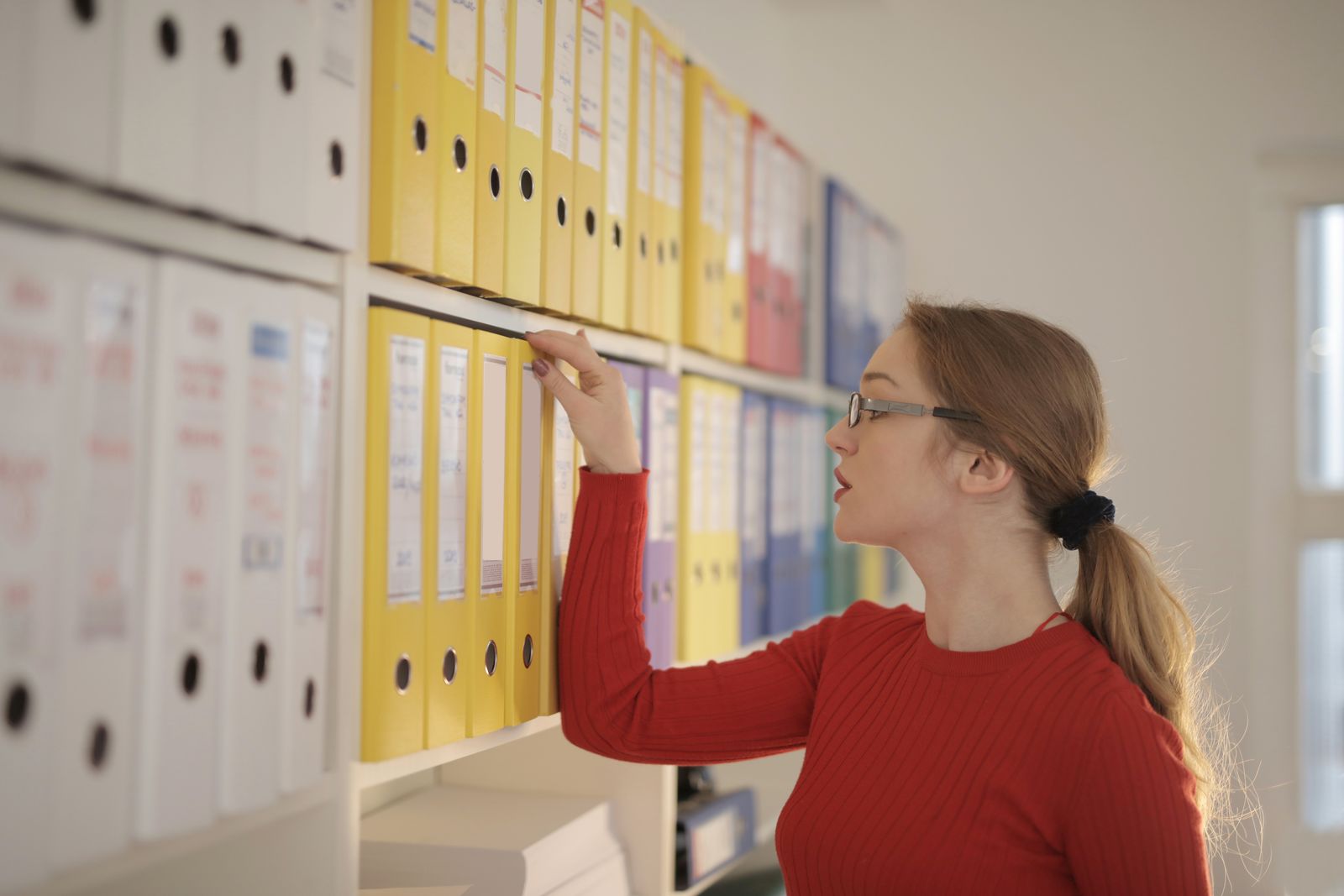 Office professional retrieving a binder from organised shelves